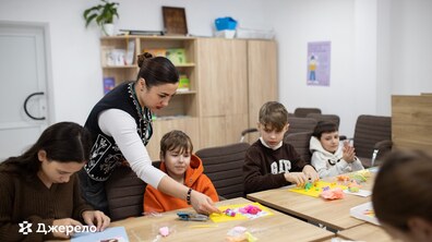 Творче заняття для дітей у навчальному просторі одного із Центрів життєстійкості у Львові. Соціальна фахівчиня допомагає дітям створювати вироби з кольорового пластиліну. Діти зосереджено і зацікавлено працюють із матеріалом, сидячи за столом.
