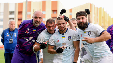Четверо учасників клубу «Покрова АМП» посміхаються та фотографуються на ігровому полі. Позаду видно житлові будинки.