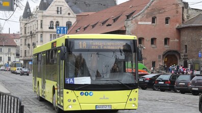 Жовтий автобус №1А їде брукованою вулицею повз історичні будинки, поруч видно припарковані автомобілі