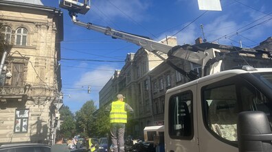 Вантажівка з автовишкою стоїть на вузькій вулиці Львова на тлі старовинних будинків. Працівник проводить роботи з кабелями, перебуваючи у люльці вишки на значній висоті.