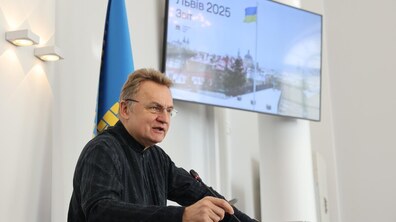 мер Андрій Садовий за трибуною в сесійні залі розповідає про підсумки роботи виконавчих органів у 2025 році. На задньому фоні екран, який ілюструє презентацію.