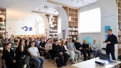 Керівник департаменту міської мобільності та вуличної інфраструктури ЛМР Олег Забарило виступає у залі перед студентами. Слухачі сидять у кілька рядів, а перед спікером на столі стоїть ноутбук із проєктором для презентації.