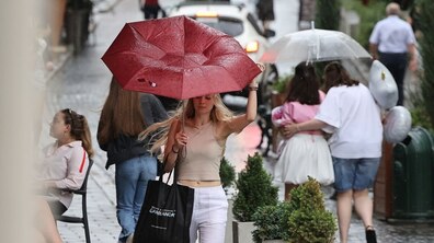 Гроза у Львові: вулицею йдуть люди під парасолями. На передньому плані дівчина, якій сильний вітер вигинає парасолю в інший бік.