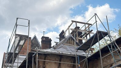 Процес відновлення будинку на вул. Мельника, 7. Вся будівля оточена високими металевими риштуваннями. На задньому плані видно фрагмент фронтону з декоративним «сонечком».