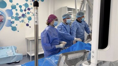 Троє лікарів у спеціальному медичному одязі – халатах, шапочках та масках, оперують пацієнта за допомогою спеціальних медичних апаратів