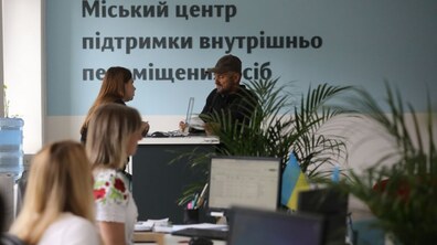 Офісний простір міського Центру підтримки внутрішньо переміщених осіб. За столом працівниця консультує відвідувача, а на передньому плані видно інших людей за робочими місцями та комп’ютерами.