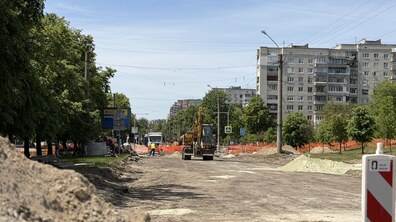 Масштабна реконструкція вул. Мазепи, де знято старий асфальт і видно лише землю та пісок. По центру дороги стоїть великий жовтий екскаватор, навколо якого працюють робітники в яскравих жилетах та складені будівельні матеріали й труби.