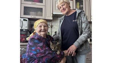 жінка літнього віку сидить на кріслі, біля неї стоїть соціальна працівниця: обоє усміхаються