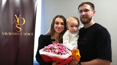 Олександр та Марічка з дитиною біля банеру із назвою своєї танцювальної студії
