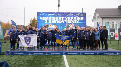 Учасники клубу «Покрова АМП» та тренери після перемоги. Спортсмени тримають у руках прапори. Позаду банер із написом 