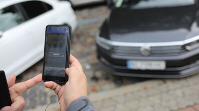 На фоні припаркованих автомобілів інспектор з паркування тримає в руках пристрій, на який фіксує порушення правил паркування