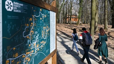 Відвідувачі прогулюються територією Шевченківського гаю, минаючи інформаційний стенд із картою локації. Люди рухаються алеєю серед дерев.