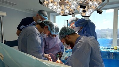 Операційна під час хірургічного втручання. Медичні працівники у стерильних халатах, шапочках і рукавичках працюють із хірургічними інструментами над пацієнтом, який лежить під яскравим операційним світлом.