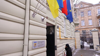 Почесне консульство Румунії біля входу якого висять три прапори: України, Румунії та Європейського Союзу. Нище - табличка із написом Почесне консульство Румунії у Львові. До будівлі заходить чоловік.