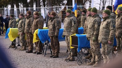 Військовослужбовці стоять у ряді. Поруч - три труни вкриті синьо-жовтими прапорами.