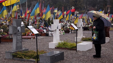 Жінка, під парасолею, розглядає три варіанти надмогильних плит, які розміщені на Личаківському кладовищі