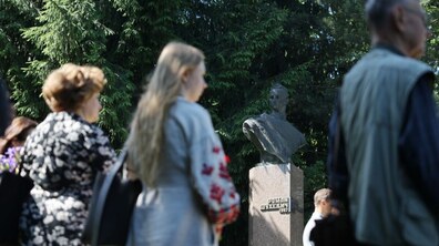 Люди стоять перед пам’ятником Роману Шухевичу під час вшанування. Позаду ростуть великі зелені ялини