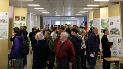 Дясятки людей в довгому коридорі оглядають карти з зображенням північного району Львова, що стоять з обох боків коридору, та спілкуються з представниками команд, які розробляли проєкти