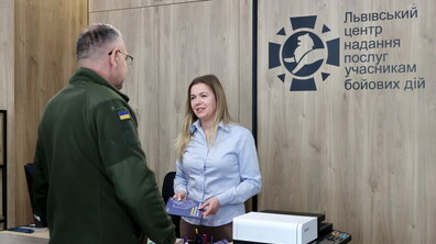 Військовослужбовець звертається до представниці Центру надання послуг учасникам бойових дій. Чоловік у формі. Жінка з усмішкою йому відповідає.