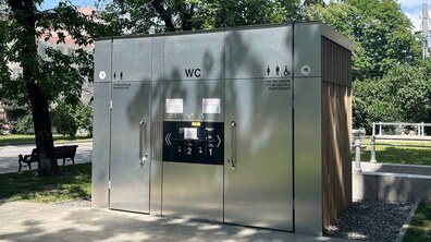 Сучасна інклюзивна вбиральня на пр. Свободи, у вигляді металевого модуля, встановленого просто неба. На передній частині напис «WC» і піктограми чоловічої, жіночої та доступної для людей з інвалідністю кабінки. Є двоє дверей із ручками та панель оплати.