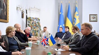 Зустріч з британськими парламентарями в кабінеті міського голови Львова. Учасники сидять за великим столом та спілкуються між собою. На столі розміщені прапорці Великої Британії та України. На задньому плані також видно прапор України, міста Львова та Європейського Союзу.