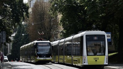 Два сучасні жовто-білі трамваї №8 рухаються містом. Навколо багато зелених дерев, а над коліями – мережа контактних дротів. Фото – ілюстративне.