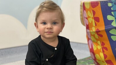 Однорічний Дем’янчик сидить на підлозі у дитячій зоні лікарні святого Миколая. Поруч видно яскравий кольоровий м’який предмет, схожий на іграшку. Хлопчик дивиться прямо в камеру з цікавістю, у нього – великі блакитні очі.