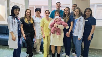 Спільне фото: у холі дитячої лікарні святого Миколая Першого медоб'єднання стоять жінка зі своїм немовлям на руках та медичні працівники, які були залучені до порятунку дитини; усі щасливі та усміхнені.