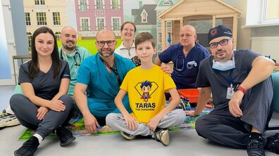 Пацієнт – 10-річний Тарас та його лікарі сидять на підлозі у холі дитячої лікарні святого Миколая; всі усміхаються