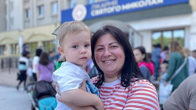 Жінка тримає на руках маленького хлопчика та усміхається, позаду – інші діти з батьками біля міської дитячої лікарні святого Миколая