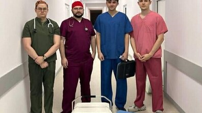 Четверо молодих чоловіків — львівських трансплантологів. Вони стоять у світлому, чистому лікарняному коридорі з білими стінами. Лікарі розташовані в одну лінію, дивлячись прямо в камеру. Перед ними на підлозі стоять спеціальні контейнери для транспортування органів.