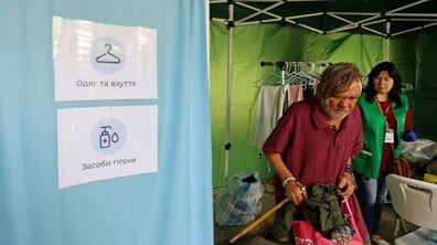 Мобільний простір підтримки, у якому чоловік обирає собі речі, а поруч соціальна працівниця допомагає йому. На наметі є напис: одяг та взуття, засоби гігієни. На задньому плані у наметі розвішаний одяг.