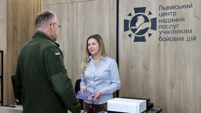 Працівниця Львівського центру надання послуг учасникам бойових дій розмовляє з чоловіком у військовій формі. В руках вона тримає «Довідник ветерана».