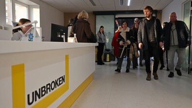 Група відвідувачів проходить коридором центру UNBROKEN повз білу стійку реєстратури з жовтим логотипом центру