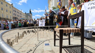 Фото з відкриття «Місця надії» на площі Ринок. По центру стоїть стілець. Навколо нього розвішані жетони з іменами. Позаду видно великий натовп людей