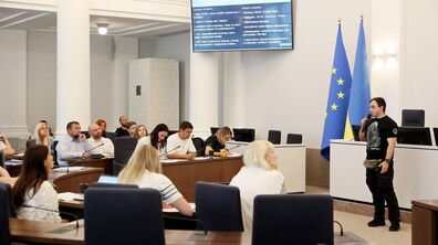 Ветеран захищає свій проєкт для отримання гранту, після проходження навчання. Зала заповнена людьми. Позаду спікера видніється екран з презентацію та прапори України і ЄС