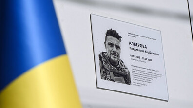 пам’ятна таблиця Герою України, полковнику Владиславу Аллерову, встановлена на світлій стіні. На таблиці розміщені його портрет, ім’я, дати життя та коротка інформація про військову службу й загибель. На передньому плані частково видно український прапор