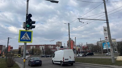 Проспект Червоної Калини. Зліва на передньому плані видно світлофор з увімкненим зеленим сигналом та знак пішохідного переходу, по дорозі їдуть автомобілі, серед яких білий мікроавтобус і синій легковик. На тлі видно багатоповерхові будівлі