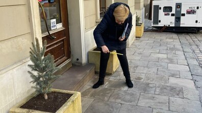 Ірина Маруняк стоїть на тротуарі перед дерев’яними дверима закладу. Вона схилилася і вимірює висоту порога за допомогою будівельної рулетки.