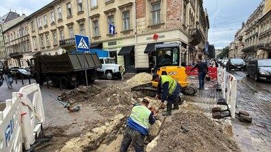 Ліквідація пориву на водопроводі на перехресті вул. Дорошенка-Костюшки. Кілька працівників Львівводоканалу працюють у розритій траншеї поруч із спецтехнікою. Ділянка огороджена захисними бар’єрами. На задньому плані видно історичну забудову, автомобілі.
