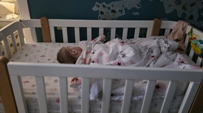 Немовля спить у дитячому білому ліжечку, позаду на стіні є наліпки у вигляді різних тваринок