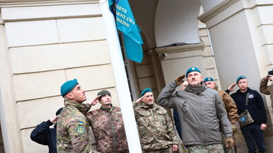 Військовослужбовець підіймає прапор на флагштоку перед Львівською міською радою. Інші військові віддають честь
