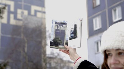 Дівчина тримає в руці розгорнутий путівник на фоні багатоповерхівок.