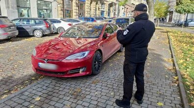 Біля червоного авто, запаркованого на тротуарі, стоїть інспектор з паркування