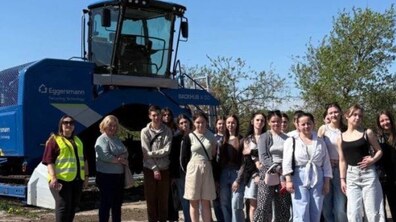 Група студентів та працівників стоять поруч із великогабаритною спеціалізованою технікою синього кольору, яка використовується для переробки органічних відходів