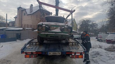 Занедбаний автомобіль на евакуаторі. Поруч стоїть чоловік