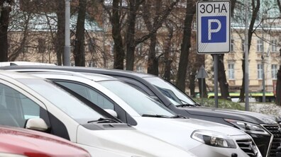 Паркувальний майданчик з автомобілями на одній з вулиць міста. Поруч видно дорожній знак, який позначає зону платного паркування, а також стовбури дерев та будівлі.