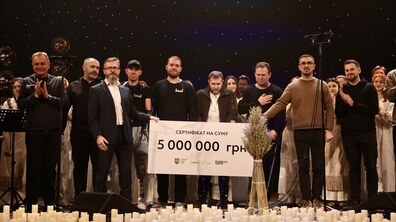 Іван Остапович, директор Львівського органного залу, та Олександр Кобзарев, виконавчий директор БФ UNBROKEN, тримають сертифікат на 5 млн по обидва боки на сцені. Поруч мер Львова Андрій Садовий аплодує. На сцені стоять представники UNBROKEN та учасники хору “Гомін”.