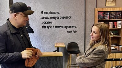 Міський голова Андрій Садовий приміряє кепки бренду «Ґвер» у крамниці. Поруч із ним стоїть Ірина, дружина Юрія Руфа. Позаду на стіні слова Юрія “Я сподіваюсь, хтось комусь озветься і скаже: він зумів життя прожить”