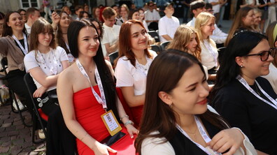 На фото учасники заходу сидять у глядацькій зоні та уважно слухають виступи. Молодь із бейджами спілкується між собою, усміхається та бере участь у програмі події, яка проходить у дворику міської ратуші.